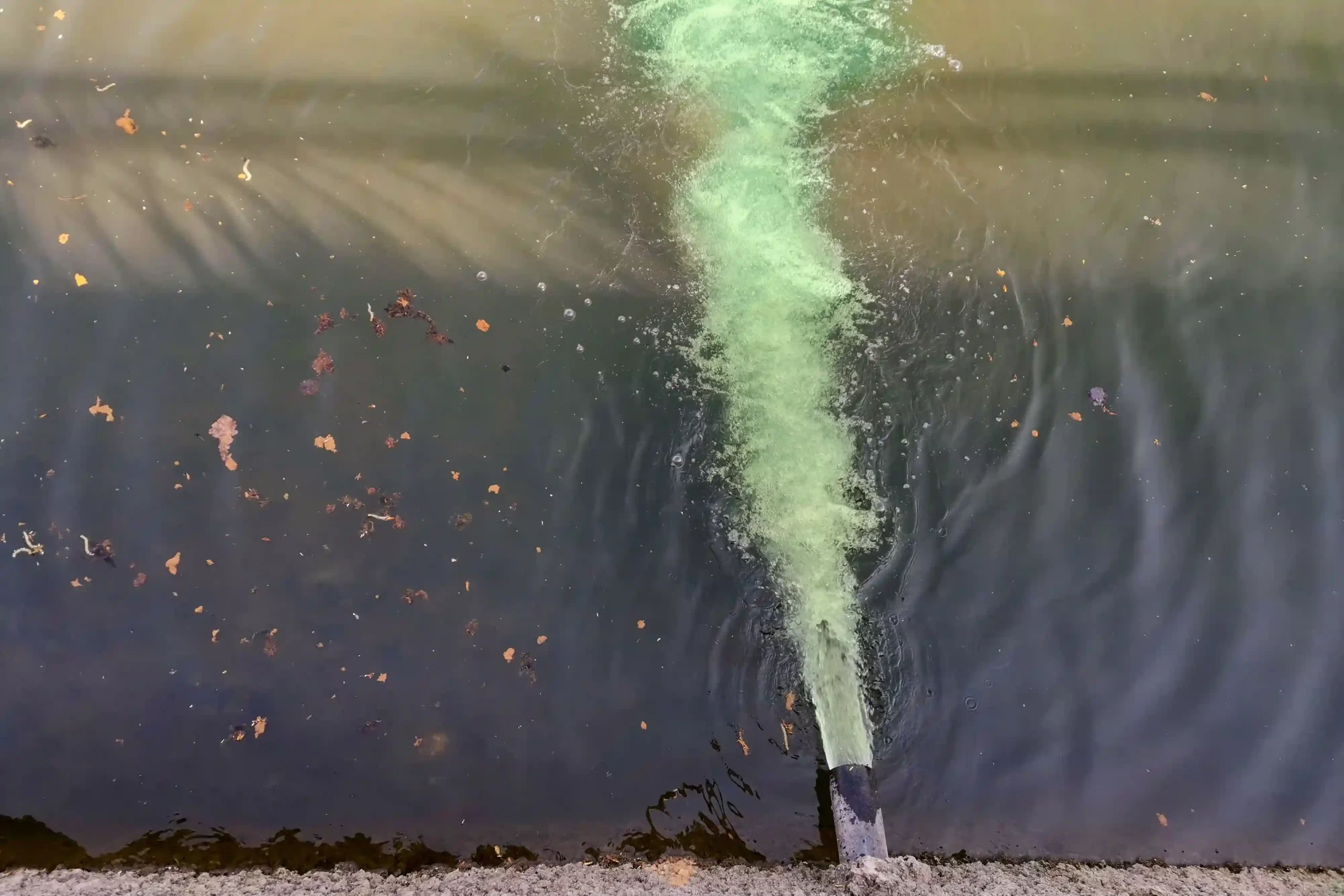 Green, polluted water being pumped into a river.