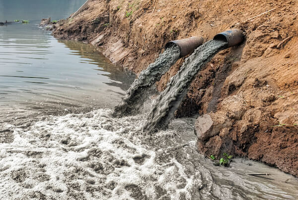 Murky, polluted waters flowing out of drains into a river untreated