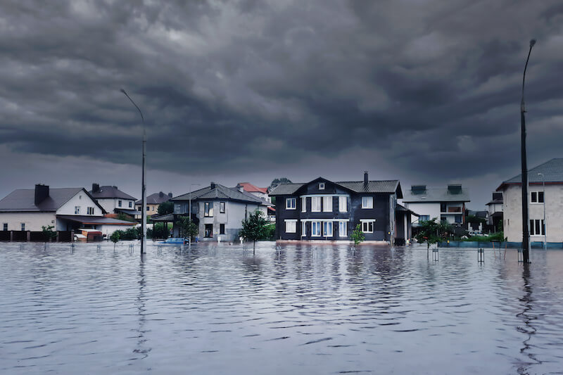 An English neighbourhood is flooded up to the the doors of people's houses, and a grey cloud looms above.