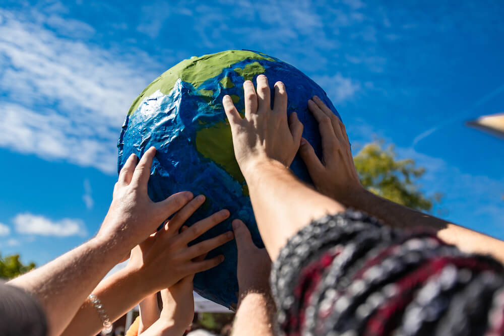 Multiple hands hold up a model of the earth as a symbol of environmentalism.