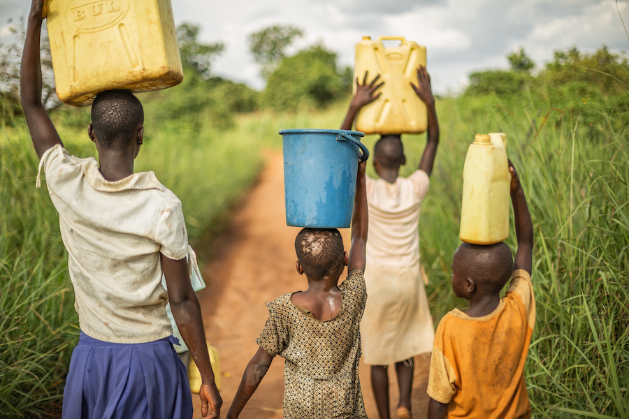 Four young African children carry buckets and jerry cans of water on their heads to take back home.