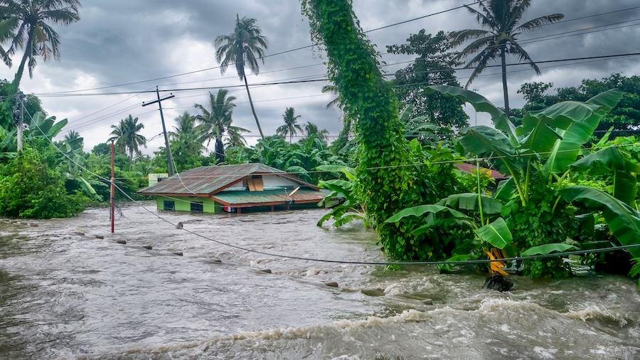 A view of a flooded street in the Philippines. A house is in view, with water up to its windows.