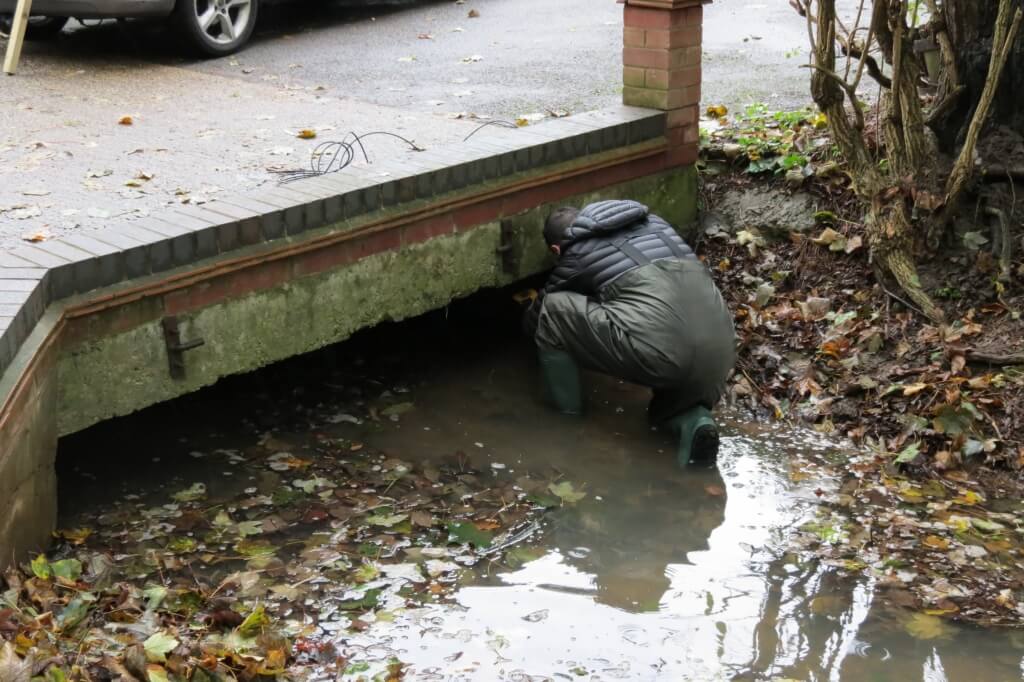 Someone in wellington boots and full rain gear is installing a Water Level sensor.