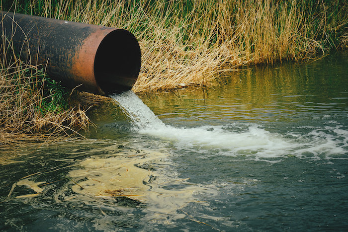 An overflow pipe over a body of water releases pollutants into the river.