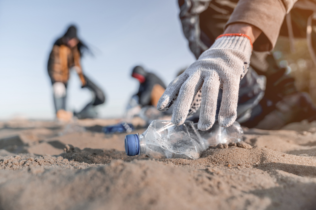 A volunteer with a glove on picks up a plastic bottle from the beach, participating in a beach cleanup.