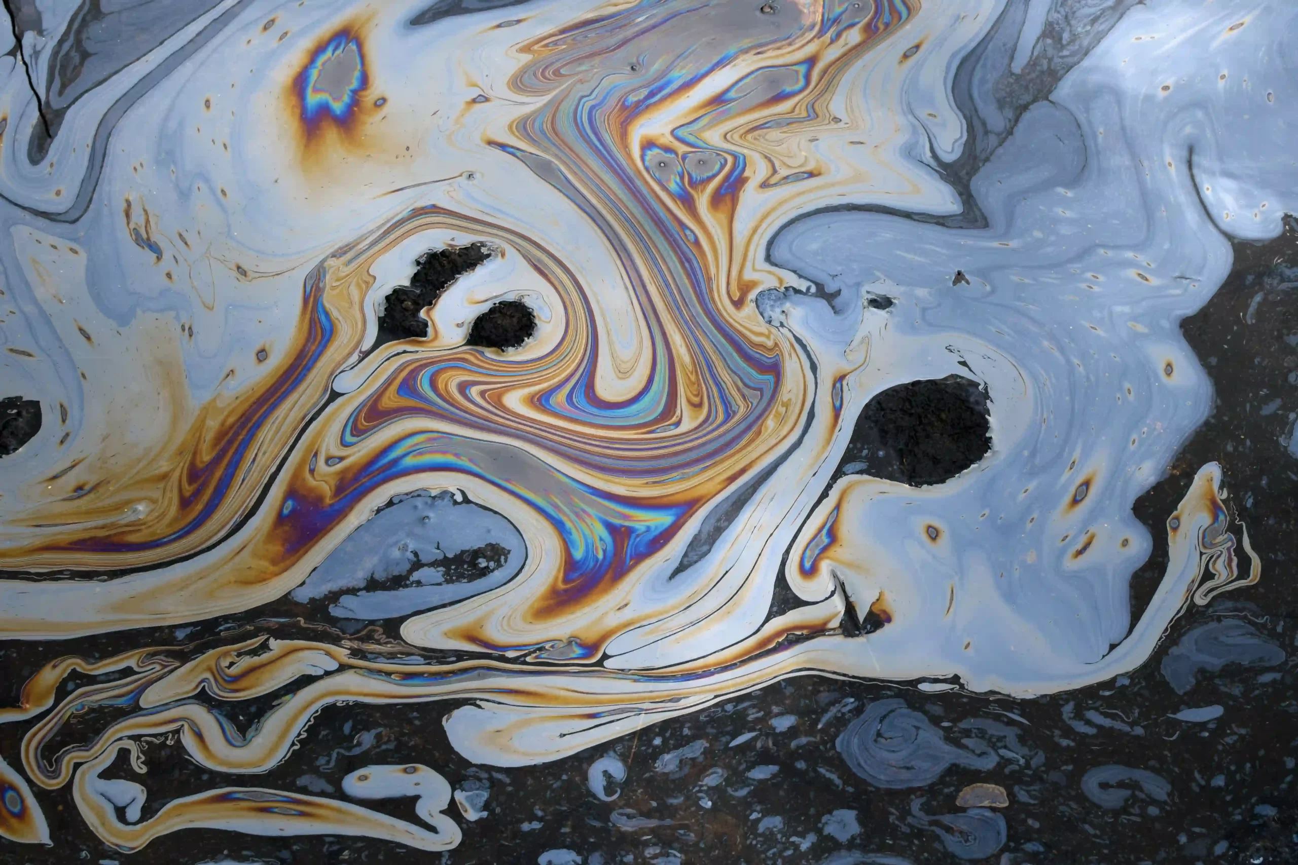 A blue, red, and orange oil slick on the surface of water, indicating chemical pollution.