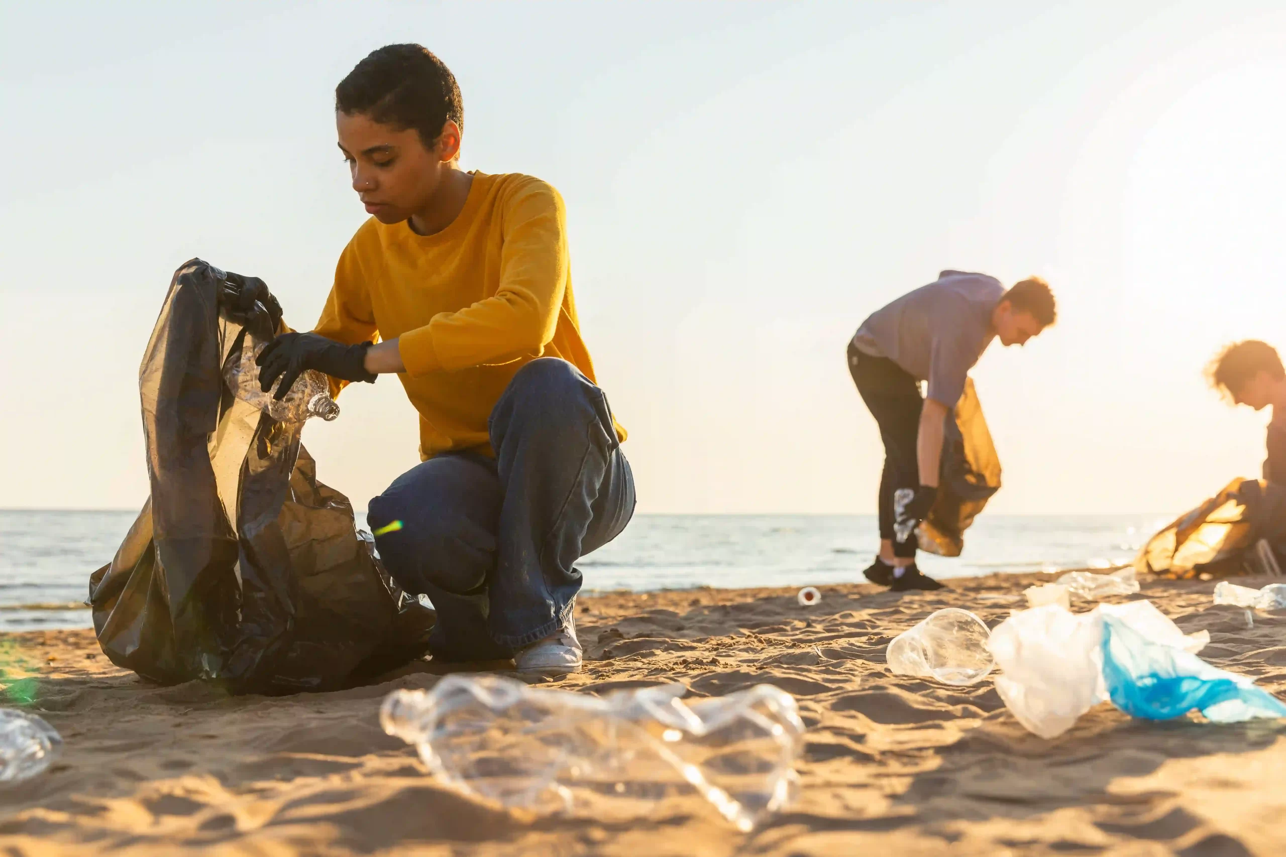 People on a beach with bin bags cleaning up plastic waste.