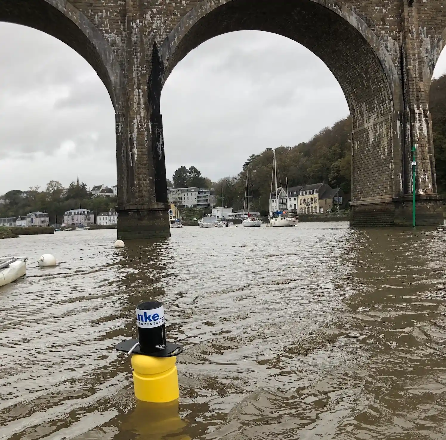 An nke Group water quality monitoring device placed in a river by a bridge.